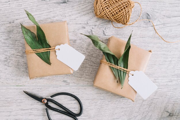 Cadeaux emballés avec étiquette et feuilles; bobine et ciseaux sur fond texturé en bois