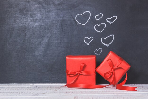 cadeaux rouges avec un tableau noir derrière avec coeurs dessinés