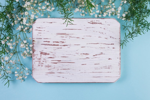 Photo gratuite cadre en bois blanc patiné blanc avec des fleurs de souffle de bébé et des feuilles sur fond bleu