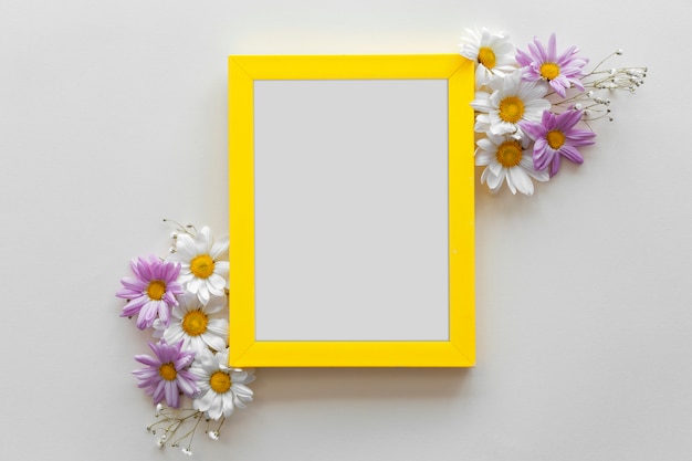 Photo gratuite cadre de bordure jaune orné de belles fleurs contre une surface blanche