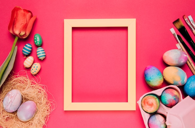Un cadre de bordure jaune vide avec des oeufs de Pâques colorés; pinceaux; tulipe sur fond rose