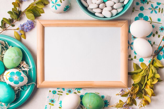 Cadre entre des oeufs de Pâques sur une assiette près de petites pierres dans un bol et des brindilles de fleurs