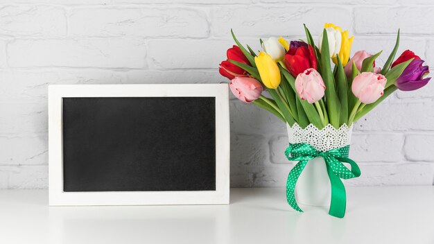 Un cadre noir vide avec vase de tulipes sur le bureau contre le mur de briques blanches