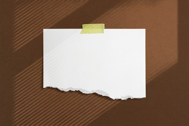 Cadre en papier déchiré vierge collé avec du ruban adhésif sur un mur texturé brun avec des ombres de fenêtre douces adobe