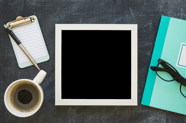 Cadre photo bordure blanche; tasse à café et papeterie sur tableau noir