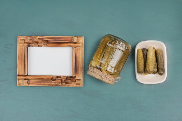 Cadre photo, concombres marinés et concombres frais sur table bleue.