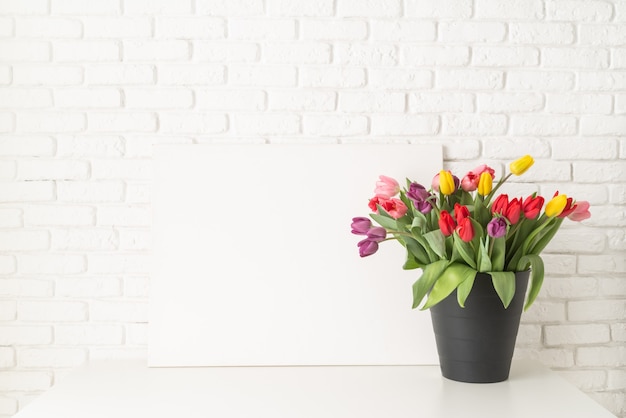 Cadre et seau de tulipes sur fond de mur de brique blanche
