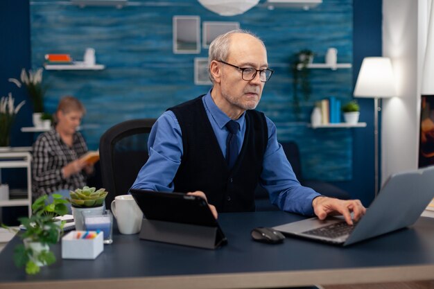 Cadre supérieur travaillant sur une présentation à l'aide d'un ordinateur portable et d'une tablette, assis au bureau