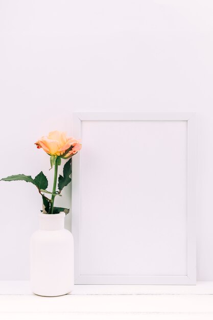 Cadre vide blanc et rose fraîche sur une table en bois