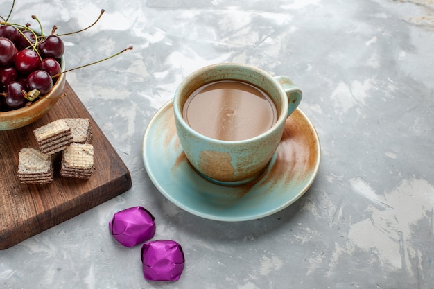 Café au lait avec des bonbons gaufres et cerises sur un bureau gris clair