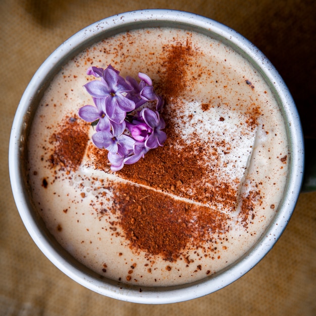 Café cappuccino dans une tasse avec des pétales de fleurs gros plan sur un morceau de sac