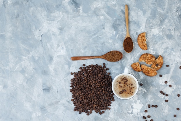 Café dans une tasse avec des biscuits, des grains de café, du café moulu vue de dessus sur un fond gris grungy