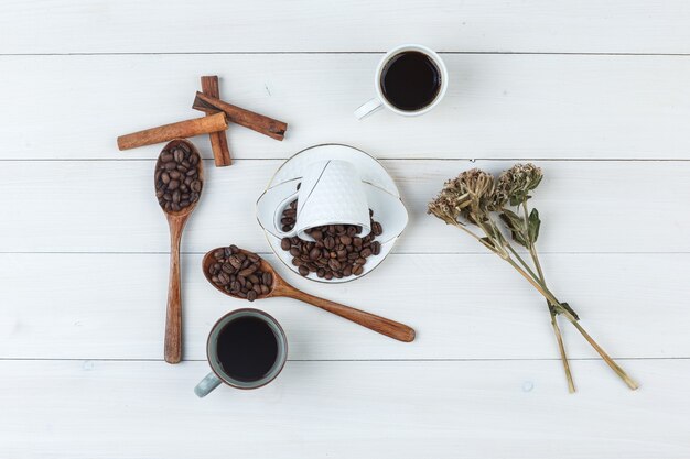 Café dans des tasses avec des grains de café, des bâtons de cannelle, des herbes séchées vue de dessus sur un fond en bois