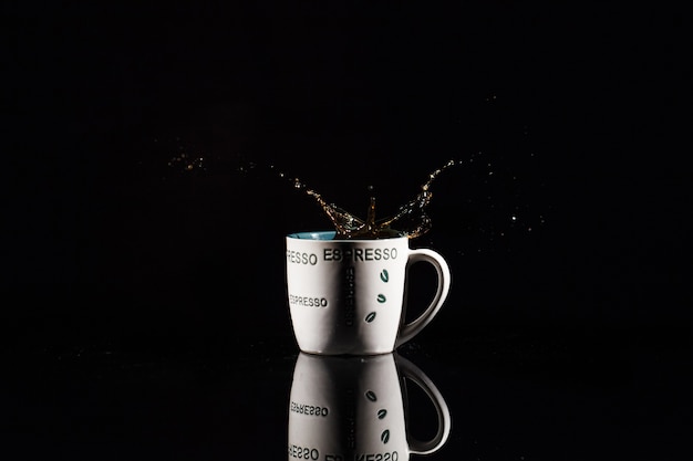 Photo gratuite café éclabousse dans une tasse blanche sur fond noir