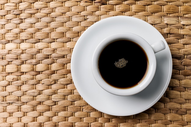 Café express classique délicieux dans une petite tasse en céramique blanche sur fond de table tissé en bois.