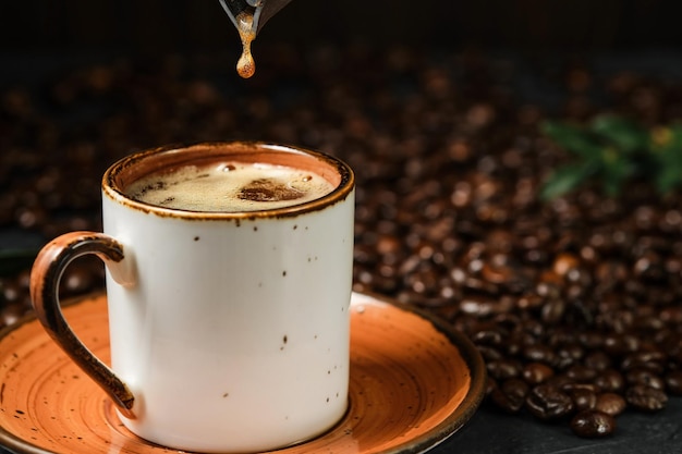 Café expresso dans une tasse en céramique blanche, gros plan, mise au point sélective. Une goutte de café tombe de la cafetière dans la tasse. Café aromatique italien pour le petit déjeuner.