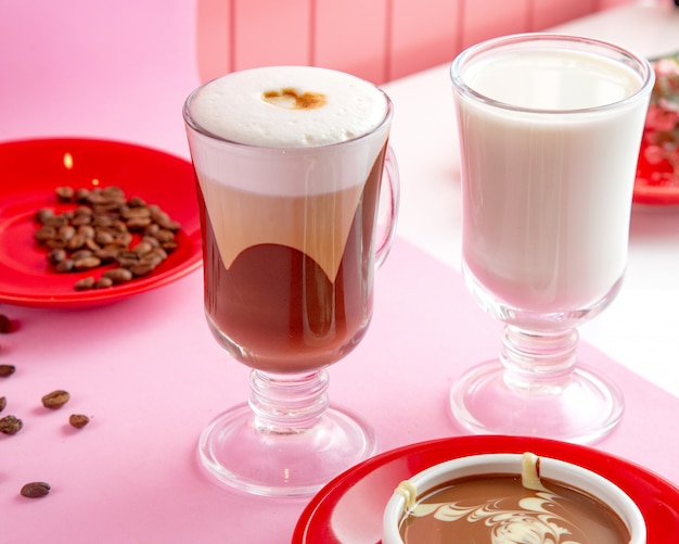 Café latte macchiato avec du chocolat au lait cuit à la vapeur et des grains de café sur la table