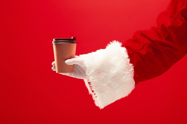 Café de Noël. La main de Santa tenant une tasse de café isolé sur un fond rouge