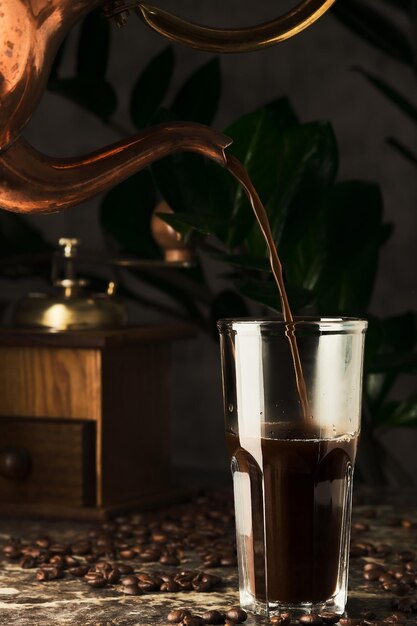 Le café de préparation du café est versé dans une tasse en verre d'une cafetière en cuivre déjeuner dans un vieux café mise au point sélective de tir vertical