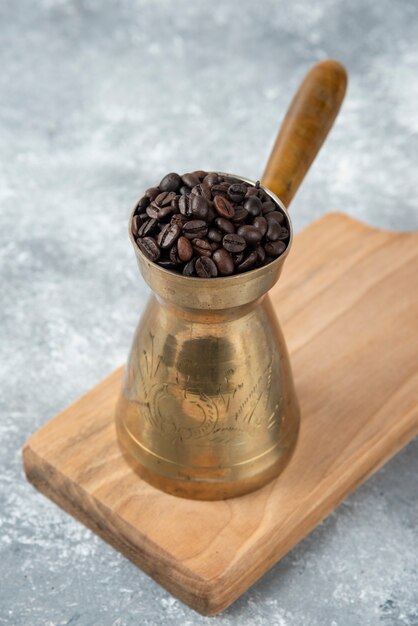 Cafetière pleine de grains de café torréfiés sur planche de bois.