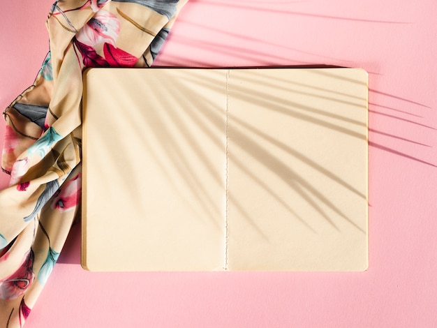 Cahier blanc sur fond rose avec une ombre de palme