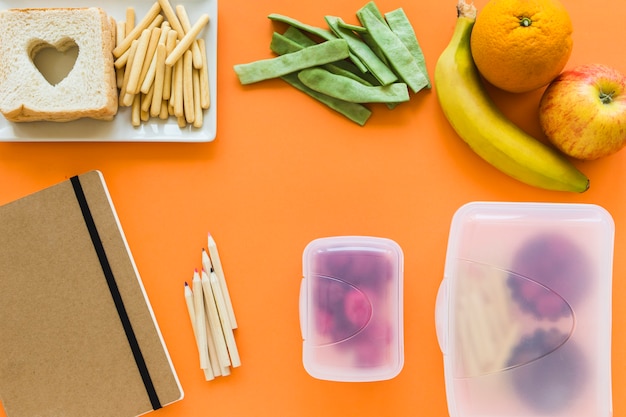Cahier et crayons près des boîtes à lunch et de la nourriture saine