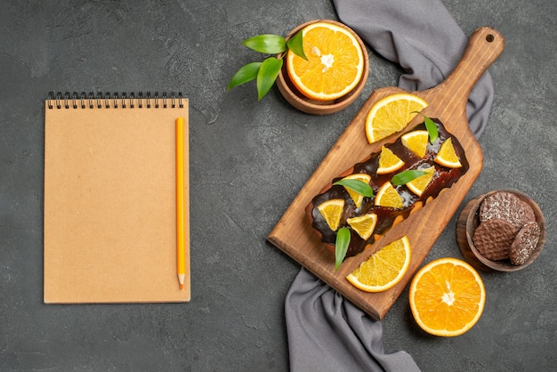 Cahier avec des gâteaux savoureux mous coupés des oranges avec des biscuits sur une planche à découper en bois et une serviette