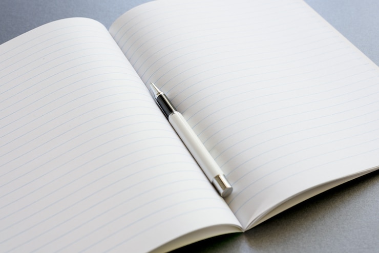 Photo gratuit un cahier ouvert avec un stylo sur un fond gris foncé, un travail de scène ou une étude.