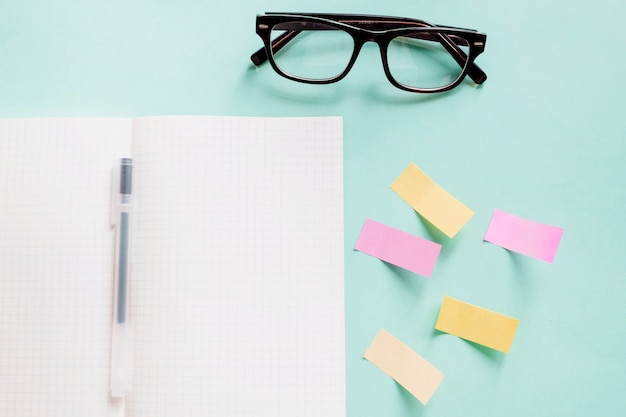 Photo gratuite cahier ouvert avec un stylo près de notes adhésives et de lunettes sur fond coloré