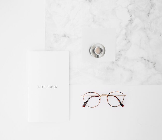 Cahier texte sur papier; tasse à café et lunettes de vue sur fond de texture blanche