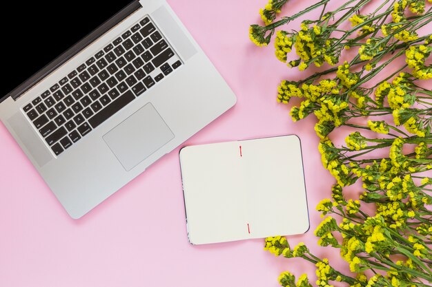 Cahier vierge; fleurs jaunes et ordinateur portable sur fond rose