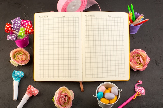 Un cahier de vue de dessus et des bonbons avec des fleurs, des bougies et des crayons sur le bonbon de composition photo couleur bureau sombre