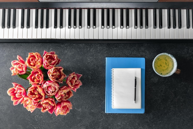 Photo gratuite des cahiers de notes de fleurs de piano et une tasse de thé sur un fond sombre en vue du haut