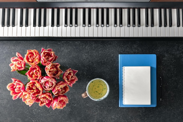 Des cahiers de notes de fleurs de piano et une tasse de thé sur un fond sombre en vue du haut