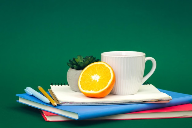 Cahiers une tasse de thé et une orange sur un espace de copie de fond vert