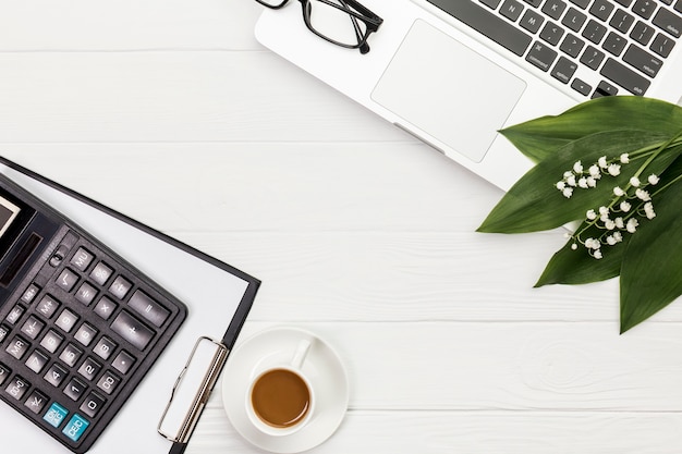 Calculatrice, bloc-notes, tasse à café, lunettes et ordinateur portable sur un bureau blanc