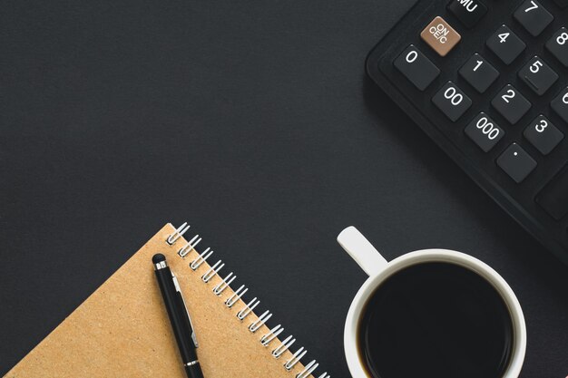 Calculatrice tasse de café et cahier sur une vue de dessus de fond noir