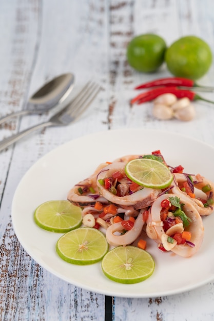 Calmars épicés au citron avec galanga, piments, carottes, menthe poivrée, oignons nouveaux et ail sur une assiette sur un plancher en bois blanc.