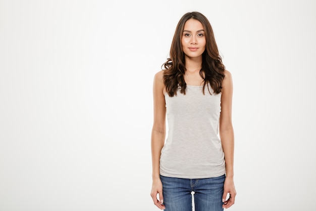 Calme femme brune qui pose en studio et regardant la caméra sur gris