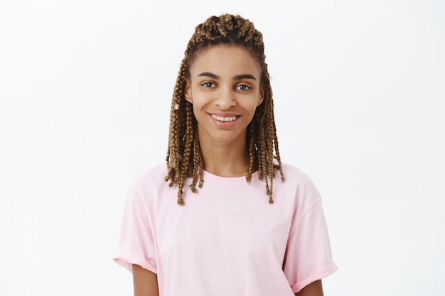 Photo gratuite calme et sympathique belle jeune femme afro-américaine avec des dreads en t-shirt élégant rose souriant assuré et joyeux