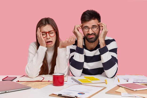 Les camarades de groupe féminins et masculins déprimés ont l'air malheureux, expriment des sentiments négatifs, s'assoient ensemble sur le lieu de travail