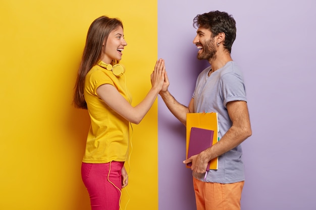 Des camarades de groupe heureux se tiennent face à face, se serrent la main, heureux de terminer la tâche commune, vêtus de vêtements décontractés, tiennent le bloc-notes pour écrire