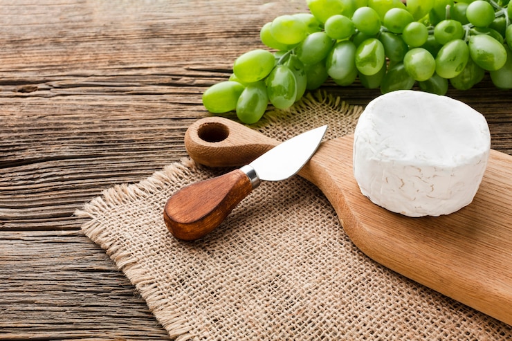 Photo gratuit camembert à angle élevé et raisins sur une planche à découper en bois