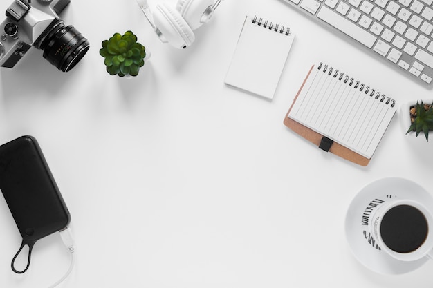 Photo gratuite caméra; banque de puissance; plante de cactus; journal intime; tasse à thé et clavier sur le bureau blanc