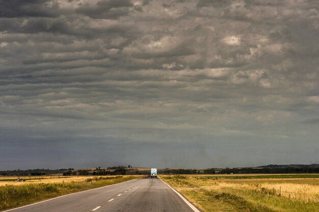 Camion sur la route entouré de champs vides sous le ciel nuageux