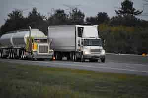 Photo gratuite camions remorques roulant sur la route entourée de beaux arbres verts