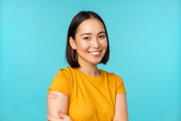 Campagne de vaccination de covid19 Jeune belle femme asiatique en bonne santé montrant l'épaule avec un concept de pansement de vaccination debout sur fond bleu