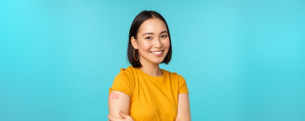 Campagne de vaccination de covid19 Jeune belle femme asiatique en bonne santé montrant l'épaule avec un concept de pansement de vaccination debout sur fond bleu