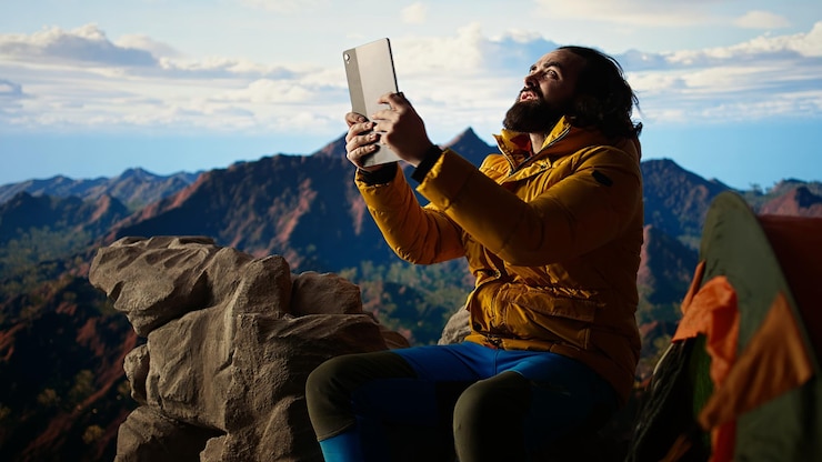 Photo gratuit un campeur luttant contre le vent fort alors qu'il utilise une tablette sur un camping en haute altitude