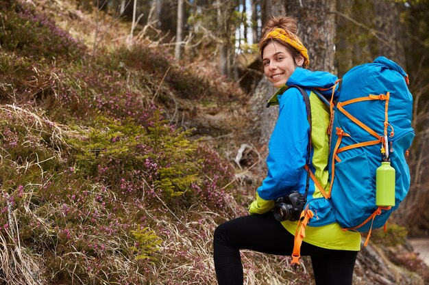 Une campeuse ravie porte un sac à dos, un appareil photo professionnel